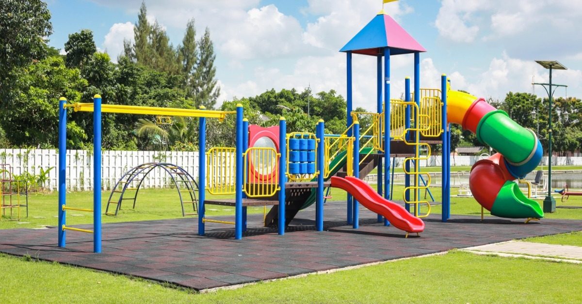 A school playground on a freshly patched rubber surface. The playground is bright colors, such as yellow, blue, and red.