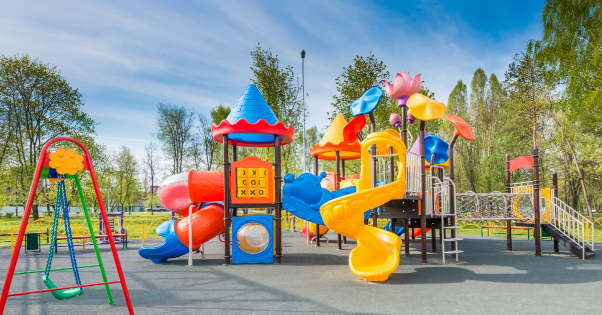 Modernizing Parks With Updated Play Features A colorful, modernized playground with swings, big slides in red and yellow, and flower petals at the top of the equipment.