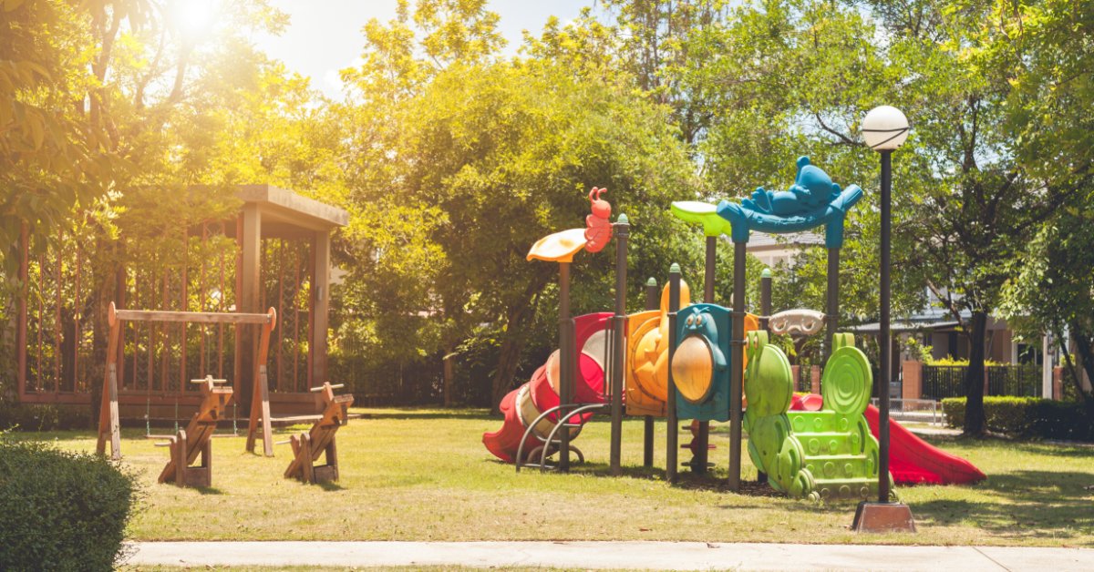 Modernizing Parks With Updated Play Features A colorful, bug inspired playground set in a patch of grass in a neighborhood. Wooden teeter totters sit on the left.