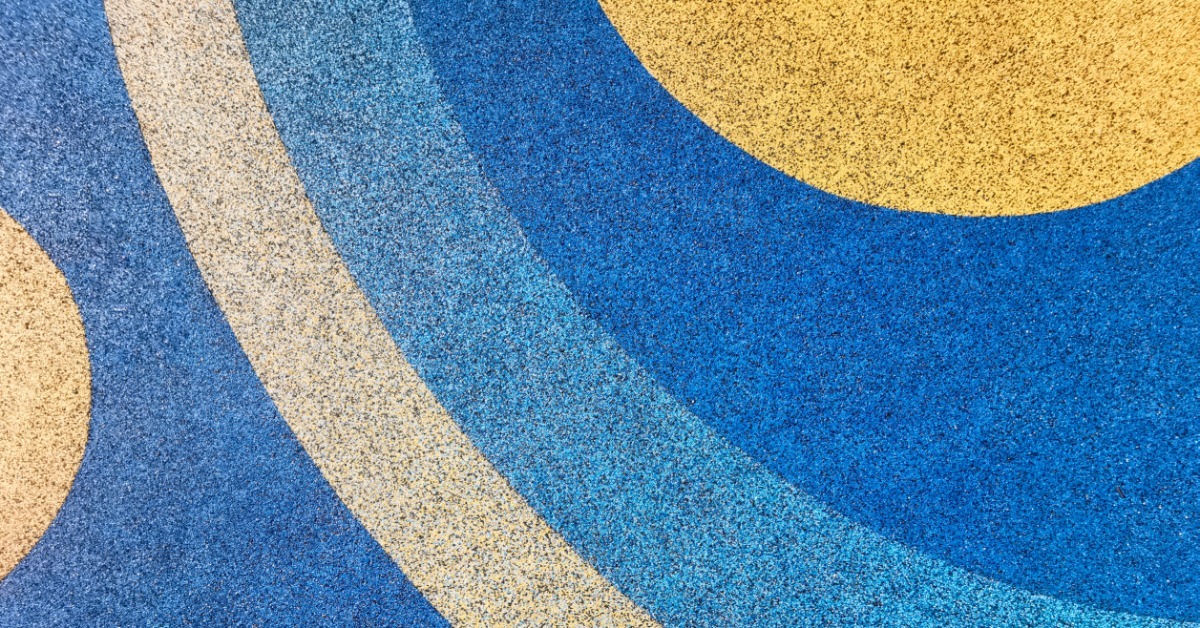 Pour-in-place rubber playground surfacing freshly laid. The blue and yellow colors make circular motions.