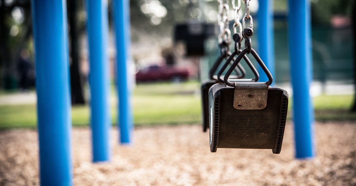 A slightly dirty swing hanging from a blue metal frame on a playground, positioned next to another swing.