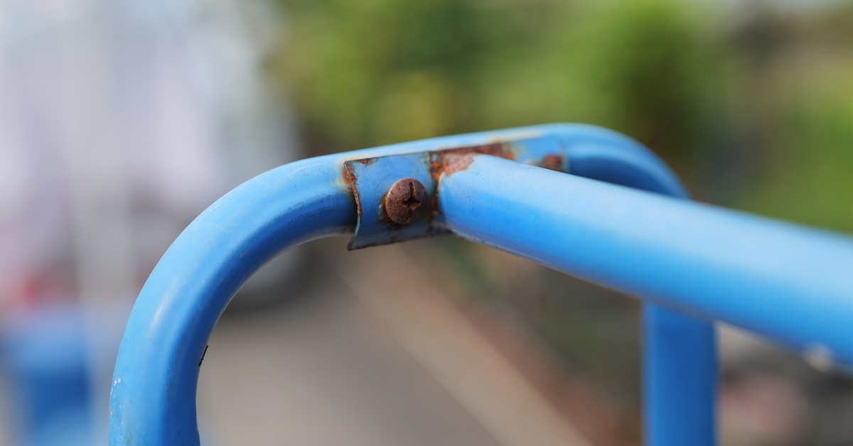 A close-up shot of a blue metal playground bar, with rust forming on a bolt and spreading around it.