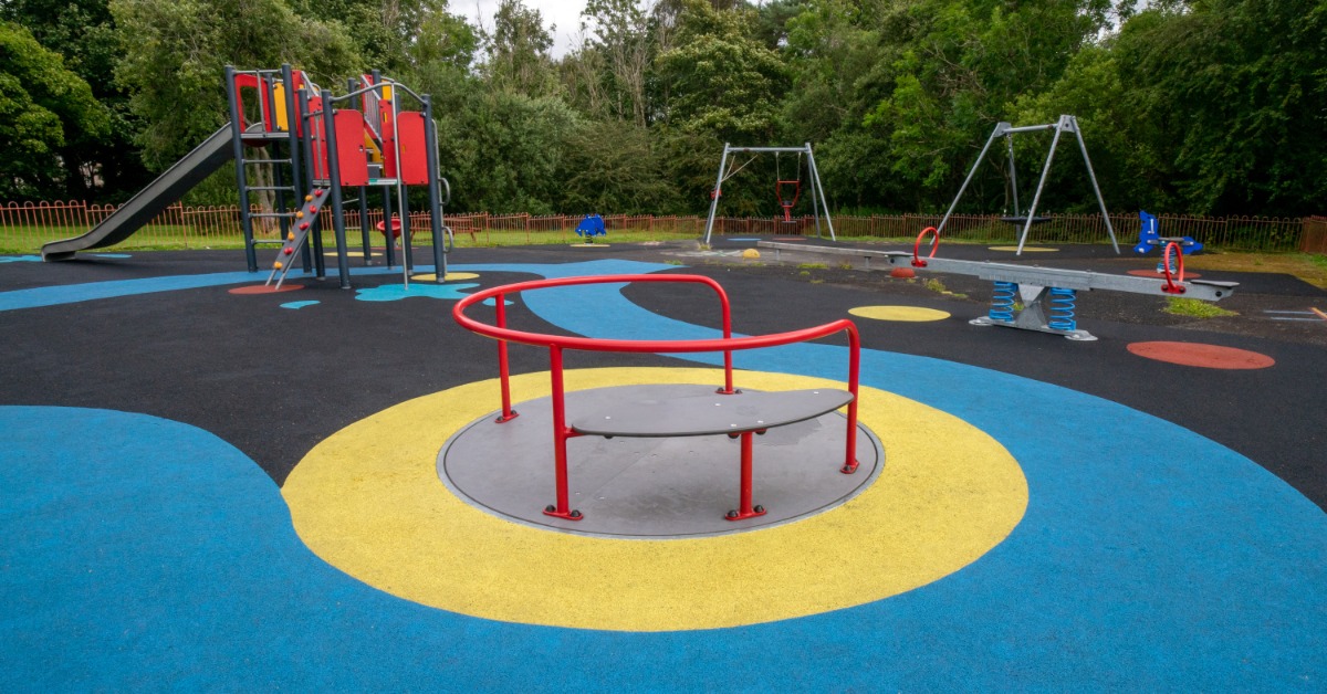 Colorful daycare playground equipment including a merry-go-round, slide, and swings on a bright rubber safety surface outdoors.