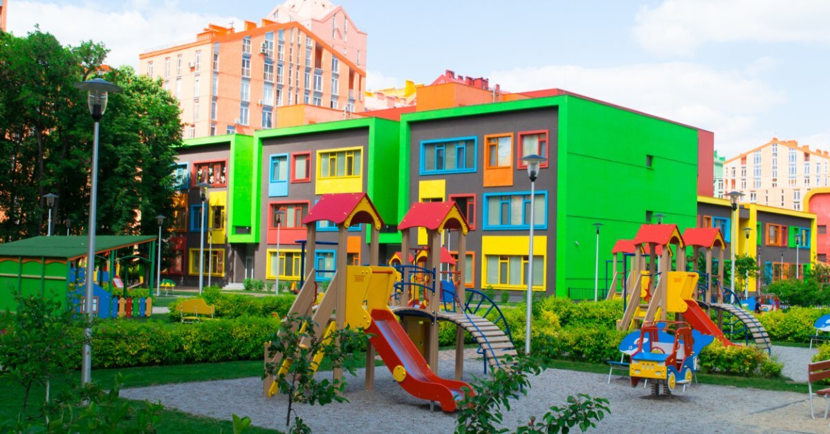 A colorful playground with slides and climbing structures in front of a bright, multicolored school building.